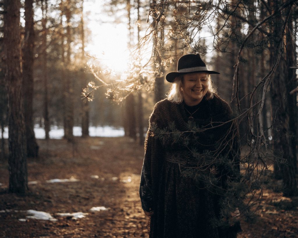 ninni-witches-north-happy-in-forest Woman lauging under a pine, sun in the bacground